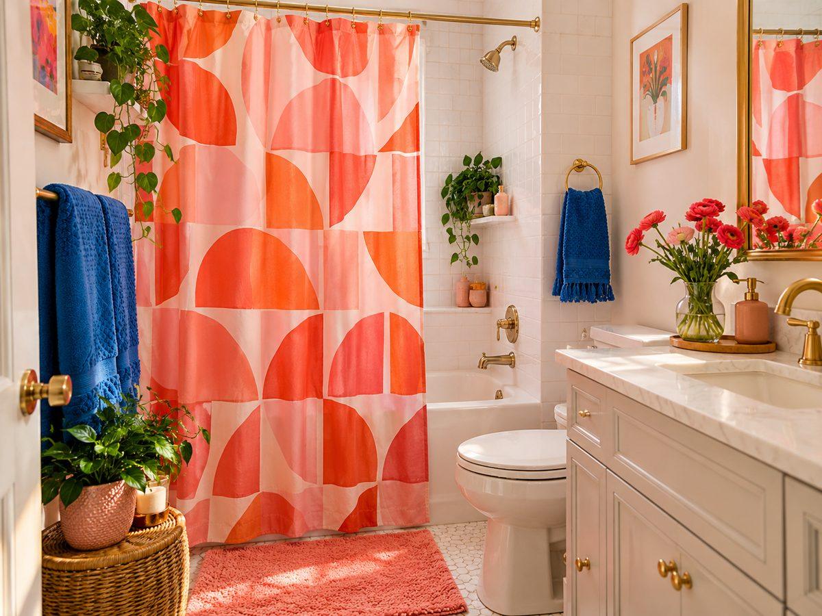Compact bathroom with a bold coral-and-pink geometric shower curtain, white tiles and blue towels